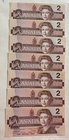 Front view of seven 1986 Canadian $2 bills showing Queen Elizabeth II portrait and denomination.