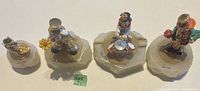 Four colorful metal clown figurines on carved stone bases, arranged in a row showing varied poses and details.