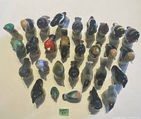 Top view showing the entire set of 27 painted clay bird figurines arranged on a white surface. Birds vary in color, shape, and species representation.