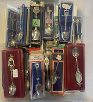 Photo showing a selection of souvenir spoons in various packages including velvet boxes and plastic sleeves.