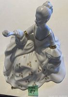 Porcelain figurine showing detailed seated woman in gold-accented dress from the front and side angle.