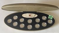 Oval presentation case open showing 12 sterling silver coins secured in place, certificate visible in the center.