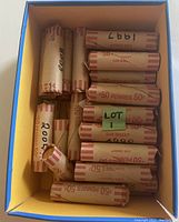 Top view of a box containing rolls of Canadian pennies with various handwritten dates on brown paper wrappers.