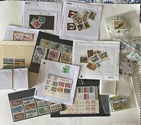 Various Canadian postage stamps arranged on a surface, including loose stamps and those in protective sheets with hole punches labeled HECO.