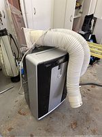 Front and side view of the black and gray Commercial Cool portable air conditioner with attached white exhaust hose.