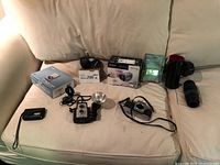 Full view of collection showing all cameras, lenses, boxes and SD cards on couch.