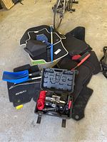 Photo showing multiple car interior mats stacked and scattered, brush and shovel handles visible, MotoMaster inflator case prominently placed at front.