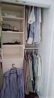 Closet view showing assorted men's shirts hanging and folded clothing on shelves