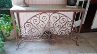 Front view of the console table showing rusty metal decorative scrollwork and granite top.