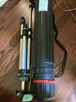 Photo of plastic black document case and tripod from top-down angle on wooden floor.