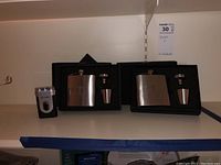 Photo showing two Welsh Rugby Union flask sets and a Bell Howdell electric shaver on a shelf.