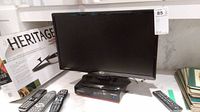 Front view of LG 22-inch TV on stand with remote control in front and a set-top box device below the TV.