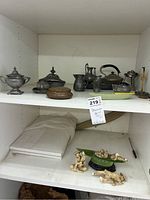 Shelf with metal teapot, several metal jugs/pitchers, and round trinket box