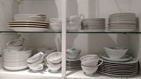 Top shelf with stacked plates and teacups, bread plates visible, some bowls below.