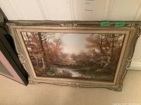 Framed landscape painting showing a river surrounded by autumn trees, measurements on sticker 27x34 and 20x27.5.