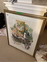 Photo of framed watercolour artwork depicting floral still life with table and framed picture inside frame, leaning against a white mantle.