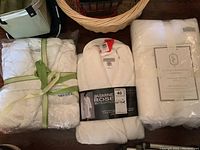 Lot with two new white terry cloth robes and a packaged set of two white bath sheets shown together on a surface.