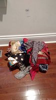 Pile of mixed scarves in various colors and patterns, some appear to be silk or satin, placed on hardwood floor.