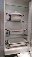 Photo showing three ceramic serving dishes of varying shapes in black metal stands on glass shelves inside a cabinet.