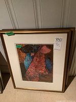 Framed mixed media artwork in gold-tone frame with white mat, with abstract colors red, blue, orange, measuring 17x12.5 inches.