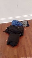Photo showing folded ski clothing items including thermal tops and pants on floor against wall.