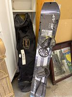 Sims ATV 160 snowboard leaning against a shelf with bindings attached and the black snowboard travel bag standing next to it.