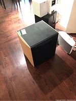 Three-quarter front view showing black grille, wood veneer side panels and matte black top surface