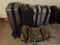 Photo showing the full set of six suitcases of various types, one canvas duffel bag, travel dolly, and a navy blue neck pillow placed on the floor against a white paneled wall.