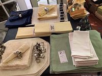 Photo showing assorted cream, green, blue, and yellow cotton napkins, placemats, and multiple metal napkin rings on a table.