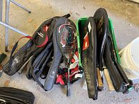 Photo showing multiple tennis rackets in cases with some loose rackets, arranged on a green crate and surrounding area in a garage or storage setting.