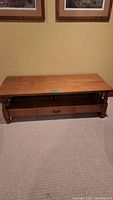 Front view of pine coffee table showing top surface, open shelf, and drawer with metal handle.