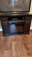 Front view of dark brown TV stand with electric fireplace insert under TV and storage compartments on the sides.