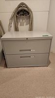 Front view of light gray 2-drawer filing cabinet with labeled drawers and lock on top drawer.
