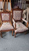 Pair of his and hers chairs, one armless, one with arms, carved wood and upholstered in patterned fabric.