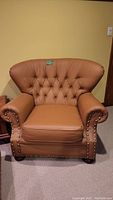 Front view of a large brown leather lounge chair with studded armrests and button tufted back.