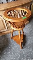 Angled side view of the wooden plant stand showing circular top and three turned legs with triangular shelf