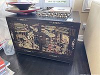 Front view of black wooden cabinet with painted Asian scene and iron hardware