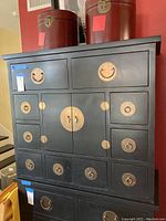 Front view of the black Asian style cabinet showing multiple drawers with brass circular hardware and central doors.