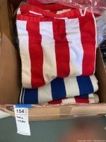 Photo of five beach towels with red and white or blue and white stripes folded inside a box, visible towel patterns and colors.
