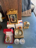 Photo of various clocks including brass carriage clock by Bulova, Vivani pocket watch, crystal golf ball clocks, and boxed wobble clocks.
