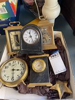 Five clocks in white box with brown packing paper: Westclox Big Ben, small marble clock, arch-top clock, carriage clock and rectangular clock