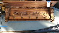 Full view of wood wall mount coat rack shelf showing five metal hooks and carved ornate detailing on the front and sides