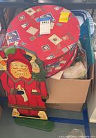 Wooden Santa Claus decoration leaning against a large round box with holiday postcard prints