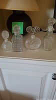 Four textured glass perfume bottles on a white cabinet with a dark lamp in the background.
