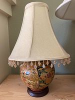 Full view of the table lamp including fabric shade with beaded fringe and painted porcelain base on wooden pedestal