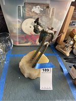 Front angle view of metal skier sculpture on stone base with ski poles and skis visible.