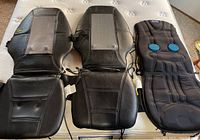 Three assorted chair back massager covers displayed on a mattress, including two black and gray Homedics Shiatsu covers and one Dr. Scholls massager with blue circular nodes.