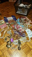 Wide view of assorted costume jewelry on wooden floor including necklaces, bracelets, earrings, and brooches.