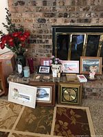 Display of multiple decor items including Royal China vase, artificial flowers (purple and red), framed nautical artwork, clock, candles and small framed photos placed on a fireplace hearth with brick background