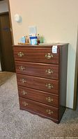 Full view of wooden dresser showing five drawers, brass handles, and wood finish.